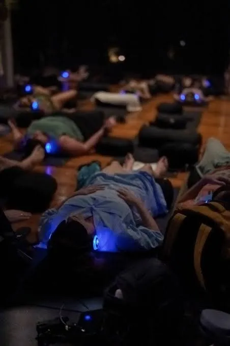 Participants lying on yoga mats using blue light headphones in a darkened studio.