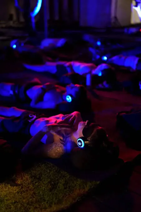 People lying on the ground wearing headphones in a dimly lit space, resting after a session.